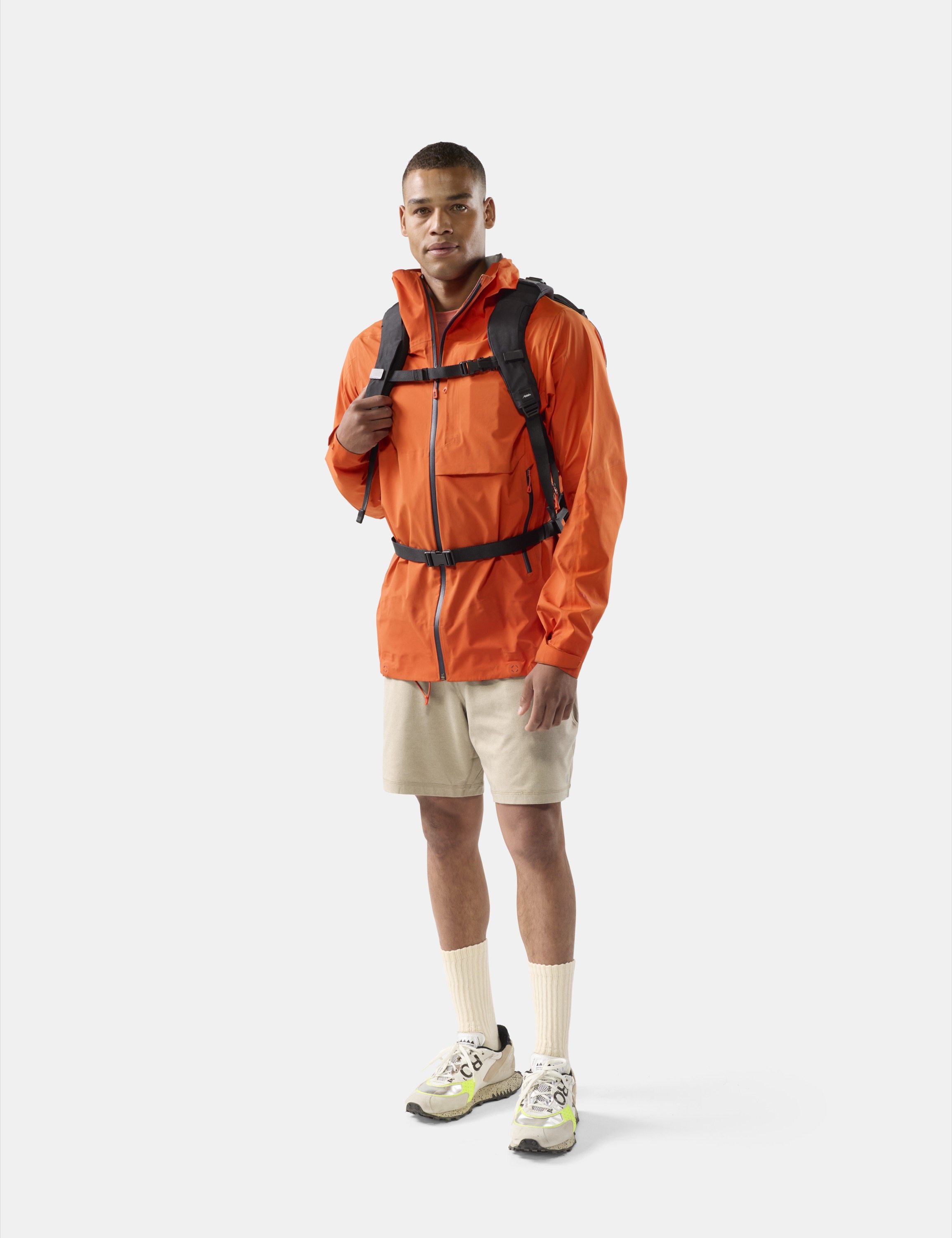 orange Jacke, Wanderjacke, Rucksackgurte, beige Shorts, Turnschuhe