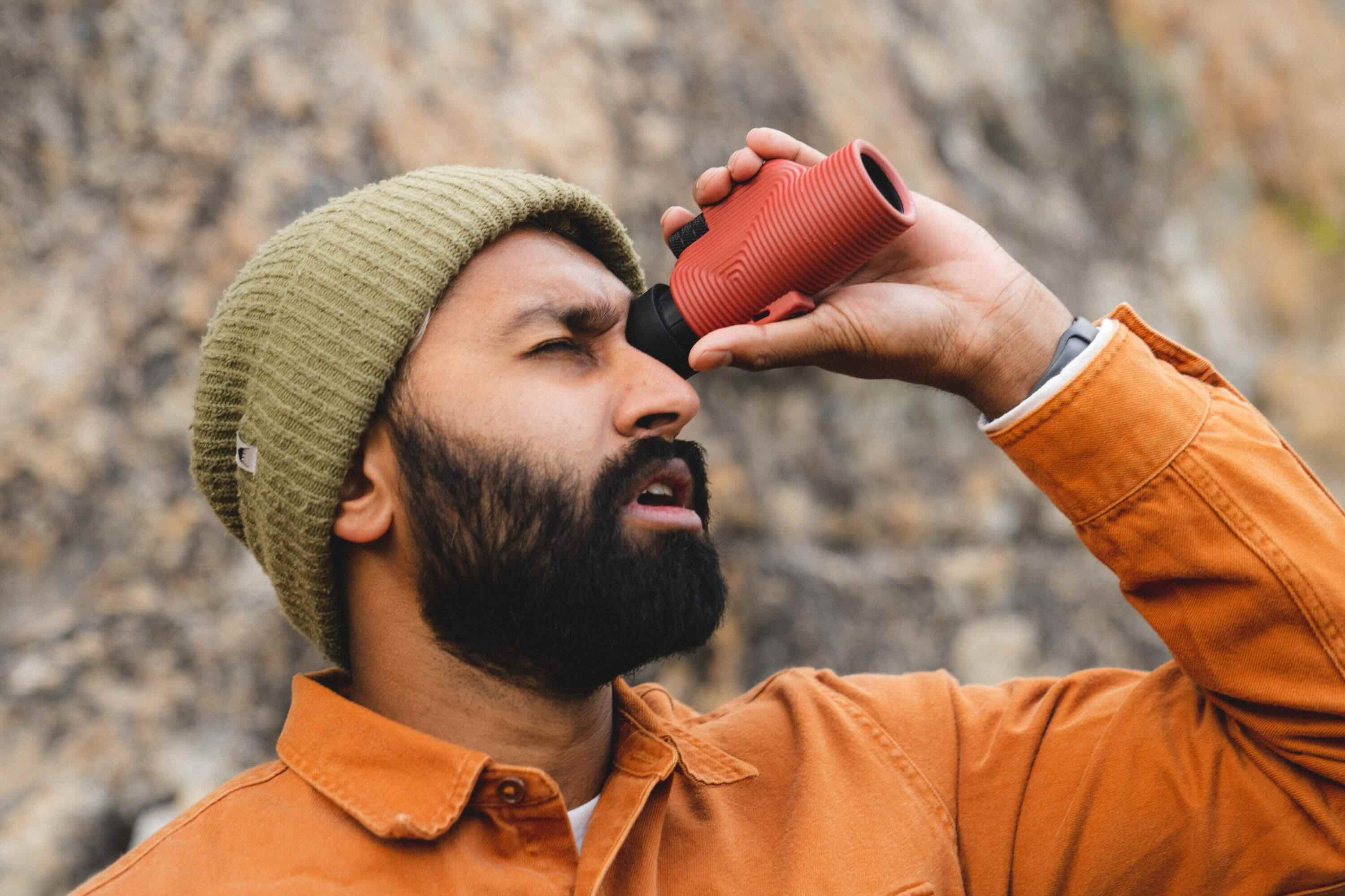 Mann, Mütze, orangefarbenes Hemd, Fernglas, rotes Gerät
